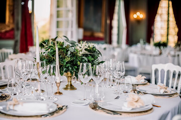 The wedding festive table is decorated with floral arrangements, glasses, plates and cutlery, the table is covered with a beautiful tablecloth