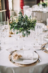 The wedding festive table is decorated with floral arrangements, glasses, plates and cutlery, the table is covered with a beautiful tablecloth