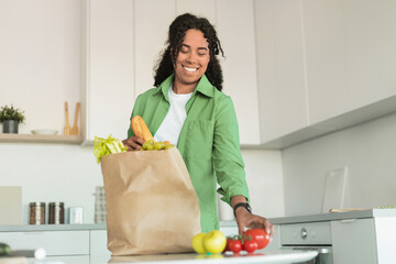 black woman unpacks paper bag of groceries in her kitchen