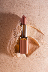 Classic nude lipstick in a gold case on a gold sand background. - obrazy, fototapety, plakaty
