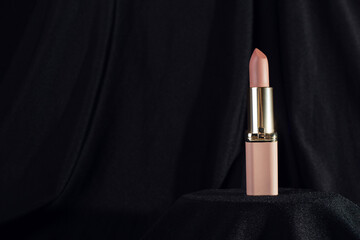 nude matte lipstick on podium on black background in a pink and gold tube top view. Professional...
