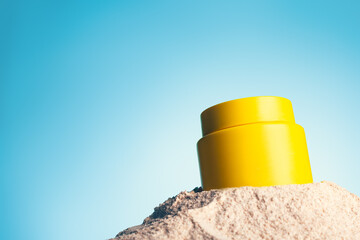 Yellow jar of cosmetic cream with lemon, vitamin c on sand and blue background. Close up, copy space.