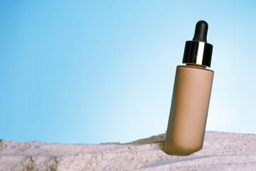 close up unbranded flacon of correction cosmetic product on blue background. Summer decorations, sand backdrop. Mockup style. Copy space in centre. Skincare and professional cosmetology concept..