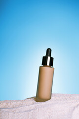 make up foundation bottle with sunscreen on blue background and sand textured background. Cosmetic products with spf. UV protection concept. Copy space mockup advertising.