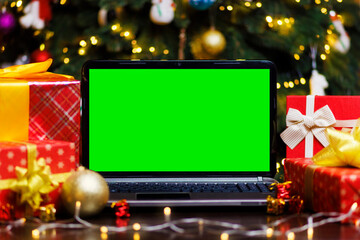 Laptop computer with green blank empty screen on table with gifts and garland