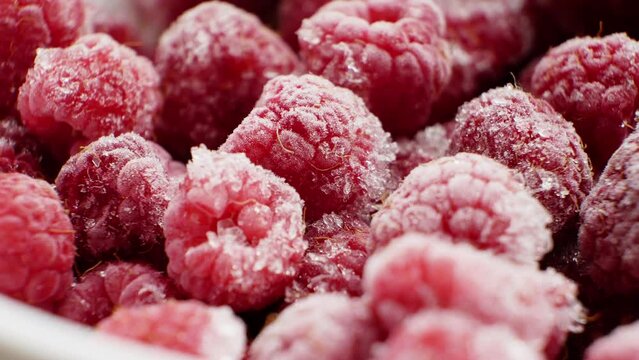 The sweetest frozen raspberries with beautiful ice and frost crystals gently swirl in a white deep plate. Preserving nutritional value with blast freezing. Aspirin. A cold remedy