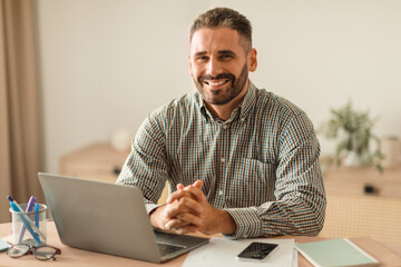 middle aged man smiling as working on laptop in office