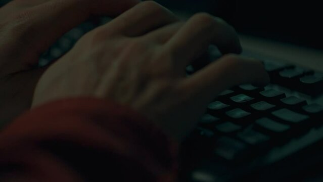 A worker at night is concentrated writing code on a portable laptop, his hands are the center of attention. Work as a programming specialist using modern equipment