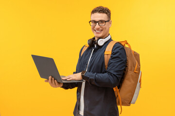 Happy young man student using laptop on yellow background