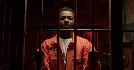 African American man in orange prison uniform comes and grabs bars of jail door
