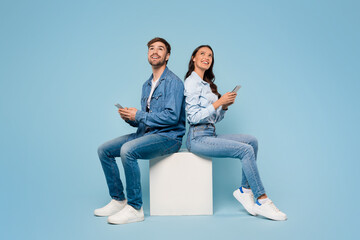 Spouses with mobiles gaze up, blue background - obrazy, fototapety, plakaty