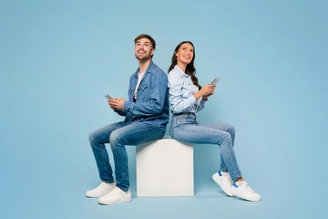 Gordijnen Spouses with mobiles gaze up, blue background © Prostock-studio
