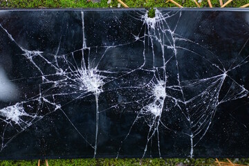 one broken large smartphone with a black screen in white cracks lies on green moss outside in nature