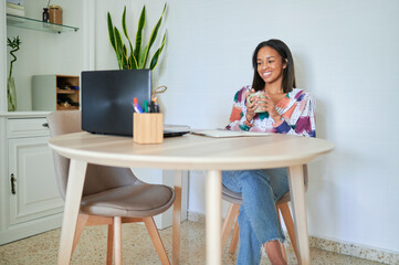 Woman with cup while looking at laptop at home