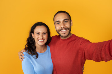 Cute positive young couple taking selfie on yellow background