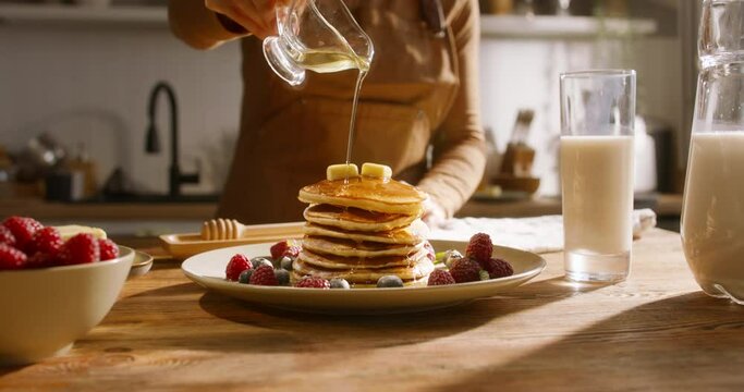 Unknown person drizzles syrup or honey over stack of perfectly arranged pancakes with berries. Advertising cinematic. Healthy lifestyle with gluten-free recipes and food options, family traditions
