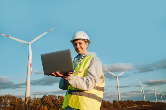 Engineer woman with laptop at wind farm during sunset