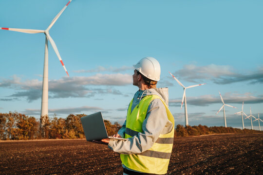 Engineer with laptop at wind farm during sunset - Powered by Adobe