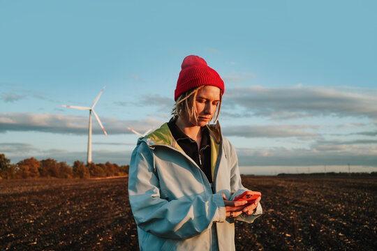 Alternative woman using smartphone in denim jacket by wind turbines