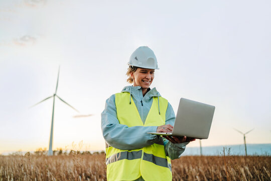 Female engineer with laptop at wind farm during sunset