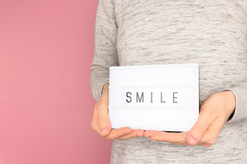 Word Smile. Female hands hold lightbox with letters in front of pink pastel background.