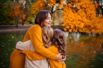 Happy family with teenagers on a walk in the park. a young mother and her twin daughters in knitted autumn clothes are having fun and hugging