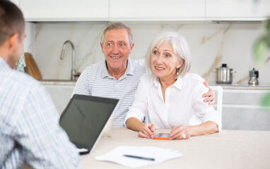 Young salesman explaining terms of deal to elderly couple sitting in kitchen. Health insurance concept