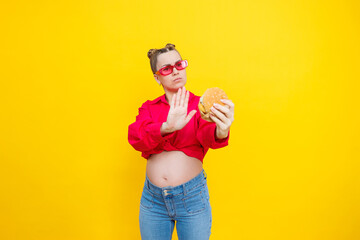 A cute pregnant woman in a pink shirt and pink glasses eats fast food. A pregnant woman on a yellow...