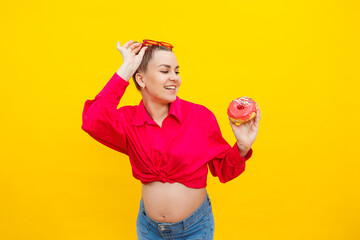 A bright pregnant woman in a pink shirt on a yellow background eats sweets. Sweet donuts in the hands of a pregnant woman.