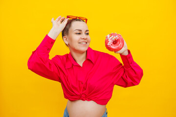 A bright pregnant woman in a pink shirt on a yellow background eats sweets. Sweet donuts in the hands of a pregnant woman.
