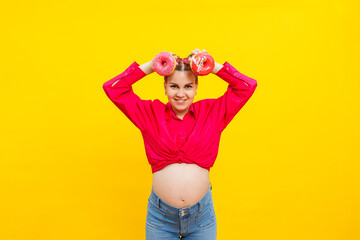 Smiling pregnant woman with sweet cakes in her hands on a yellow background. Delicious sweet donuts...