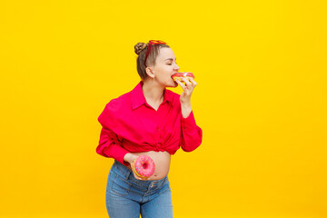 regnant woman eats sweet donuts on a yellow background. A pregnant woman in a pink shirt and glasses eats a sweet cake. Harmful food during pregnancy.