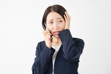 スマートフォンで電話をしながら頭を抱える中年のビジネスウーマン　白背景