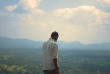 Man wearing a mask overlooking the mountains in Pidurangala Rock (Sigiriya)
