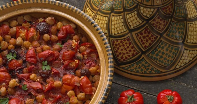 Moroccan vegan tagine made of Ethiopian eggplant and chickpea in an open traditional tagine pot. A few Ethiopian eggplants next to it. Top view, table spin.