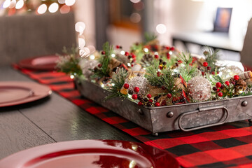 Decorated Centerpiece on a wooden table with Christmas settings and Christmas decorations and lights in the background.