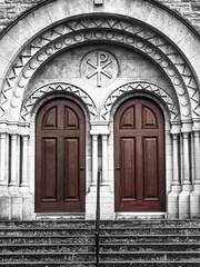 Vertical shot of a stone building with two brown doors and the Christian symbolism on top
