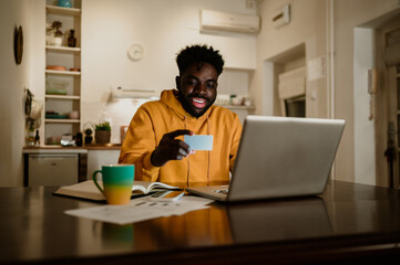 A cheerful interracial man is using a credit card for shopping on the internet on his laptop.