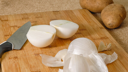 Fototapeta na wymiar Peeling and cutting white onion on a cutting board. Vegetable soup recipe. Ingredients close-up