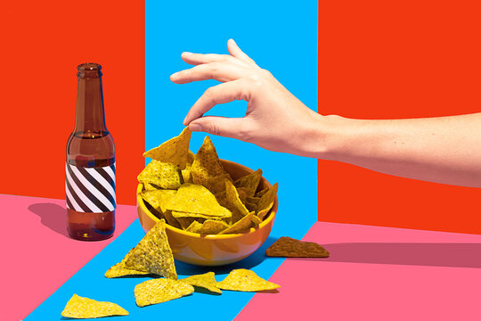 Unrecognizable hand picking nachos with colorful backdrop