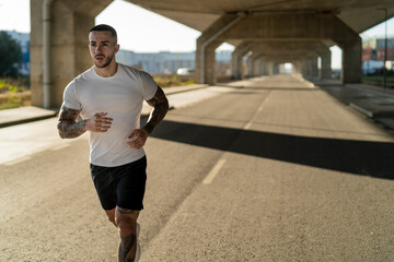 Chico joven musculoso y tatuado haciendo ejercicio y usando smartphone en carretera