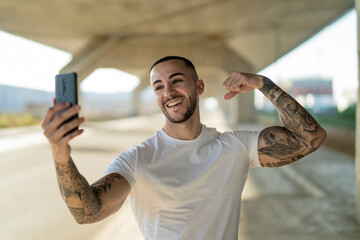 Chico joven musculoso y tatuado haciendo ejercicio y usando smartphone en carretera