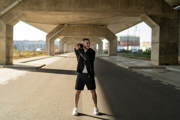 Chico joven tatuado y musculoso posando y haciendo deporte en la calle en un tunel con un puente de...