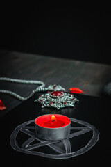 Black leather book with a magical sign, an amulet and a candle, on a black background.