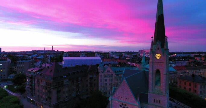 Aerial Backward Shot Of Lutheran Church Amidst Buildings Against Pink Sky - Stockholm, Sweden