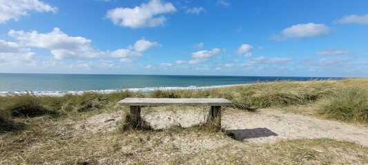 Panoramic shot of the sandy beach with a chair by the blue sea under a blue sky