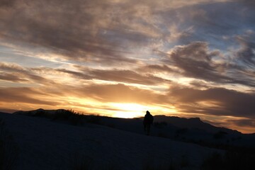 Fototapeta premium Scenic view of a person in the snowy field watching the mesmerizing sunset in the cloudy sky