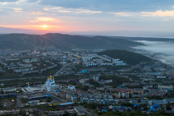 Fototapeta na wymiar Morning cityscape. Top view of the cathedral, buildings and streets. Residential urban areas at sunrise. Fog over the ground. City of Petropavlovsk-Kamchatsky, Kamchatka Krai, Far East of Russia.