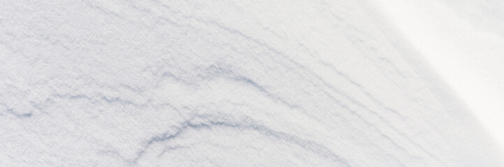 Beautiful winter background with snowy ground. Natural snow texture. Wind sculpted patterns on snow surface. Wide panoramic texture for background and design. Closeup top view with copy space.