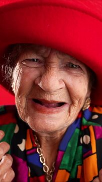 Vertical video of unhappy displeased fisheye portrait caricature of funny elderly woman saying NO with red hat isolated on red background.